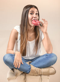 Portrait of young woman eating donut against white background
