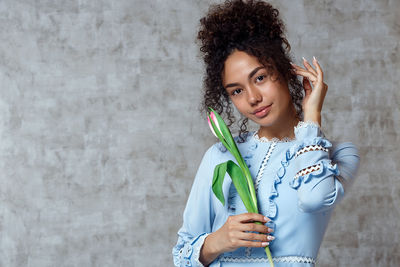 Portrait of smiling young woman holding tulip while standing against wall