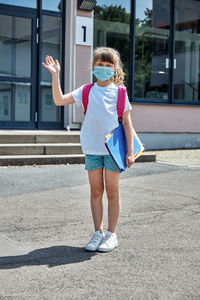 Back to school. a schoolgirl, a girl stands next to the school and waves her hand.