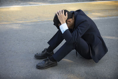 Side view of mid adult man with head in hands sitting on road