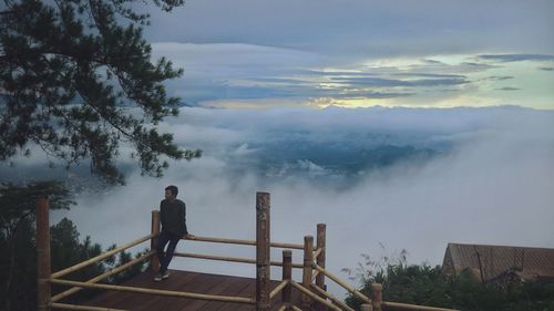 Rear view of man standing by railing against sky