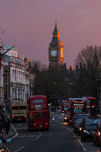 Vehicles on street against big ben at sunset