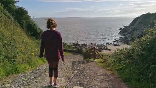 Rear view of woman standing by sea against sky