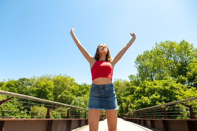 Full length of happy woman standing by tree against sky