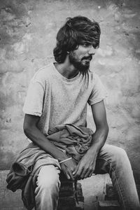 Young man looking away while sitting on wall