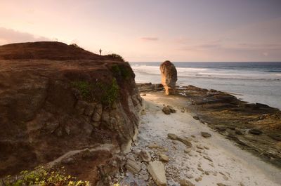 Rocks on beach against sky during sunset