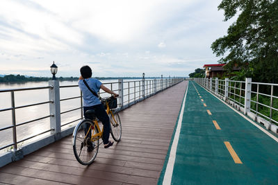 Rear view of man riding bicycle by railing against sky