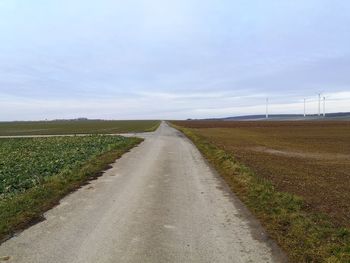 Empty road amidst field against sky