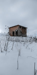 House on snow covered field by building against sky