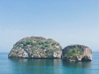 Rock formation in sea against clear blue sky