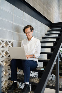 Focused male worker with netbook sitting on staircase while working in light modern workspace during work