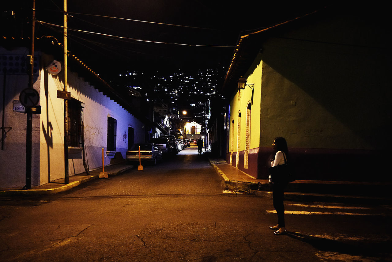 architecture, night, illuminated, building exterior, built structure, city, real people, street, one person, full length, building, the way forward, lifestyles, direction, transportation, road, footpath, outdoors, men