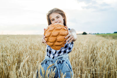 Teenager girl holding loaf of bread while standing amidst farm