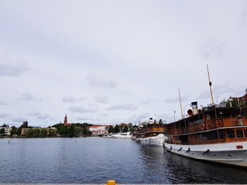 Sailboats moored on river by buildings against sky