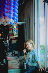 Smiling woman talking on phone while standing by window