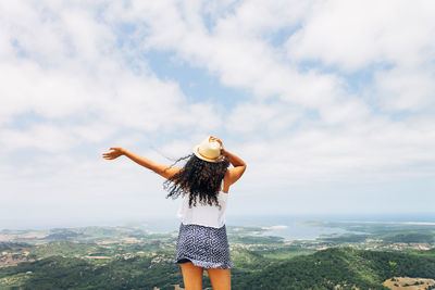 Young woman with arms outstretched standing on landscape against sky