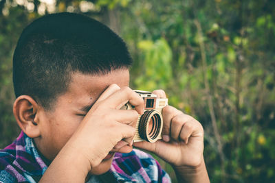 Close-up of boy photographing through camera against plants