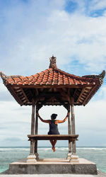 Rear view of man sitting at sea against sky