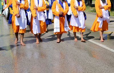 Sikh men dressed in traditional orange, white and blue clothes walk barefoot at a parade
