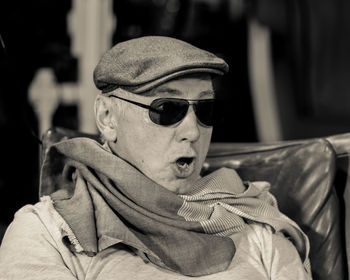 Close-up of senior man in sunglasses and cap making face while sitting on chair