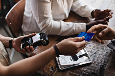 Cropped image of man giving credit card to waiter at table in restaurant