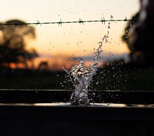 Close-up of water splashing by fence against sky