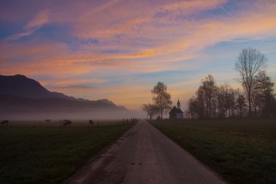 Empty road amidst field against sky during sunset