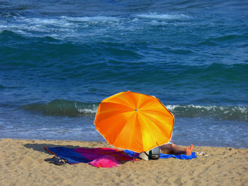 Person resting by yellow parasol on sea shore at beach during sunny day