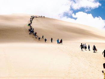 People walking on desert against clouds