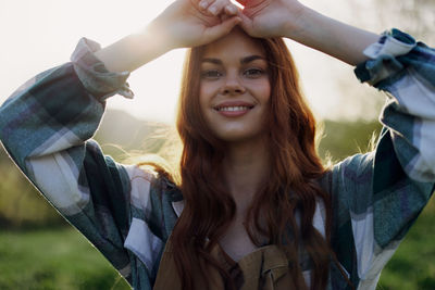 Portrait of young woman with arms raised standing against sky