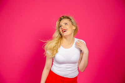 Portrait of a smiling young woman standing against pink wall