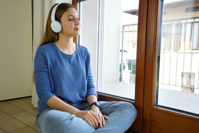 Smiling woman listening music while sitting by window