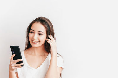 Portrait of smiling young woman using smart phone against white background