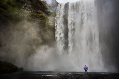Rear view of person standing by waterfall
