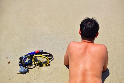 Rear view of shirtless man lying on sand