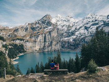 Rear view of women sitting by lake against sky