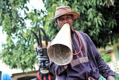 Portrait of man holding sound equipment while standing against tree