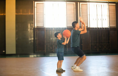 Side view of father playing basketball with son in court