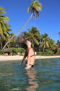 Man in mid-air by palm tree against sky