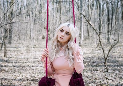 Portrait of a beautiful young woman swinging in swing in forest