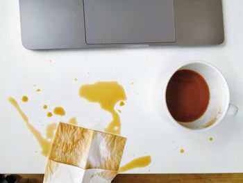 High angle view of spilled coffee and cup on desk and laptop