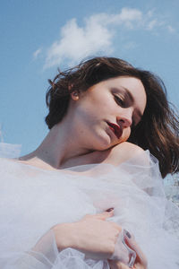 Low angle view of young woman in white dress against sky