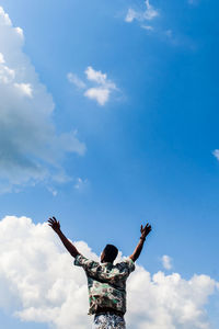 Rear view of man with arms raised against sky