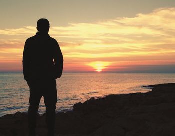 Silhouette man standing on beach against sky during sunset