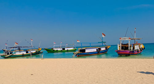 Boats moored on beach against clear blue sky