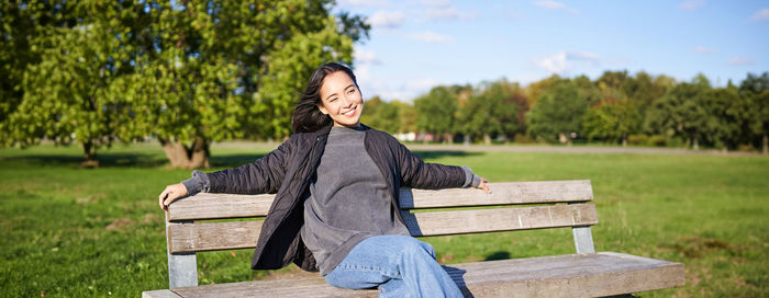 Portrait of young woman sitting on bench against trees