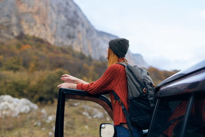 Rear view of man sitting on mountain against sky