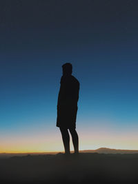 Silhouette of man standing on landscape at sunset