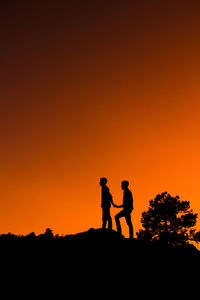 Silhouette men standing against orange sky