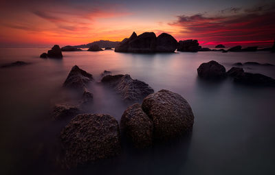 Rocks in sea against orange sky during sunset